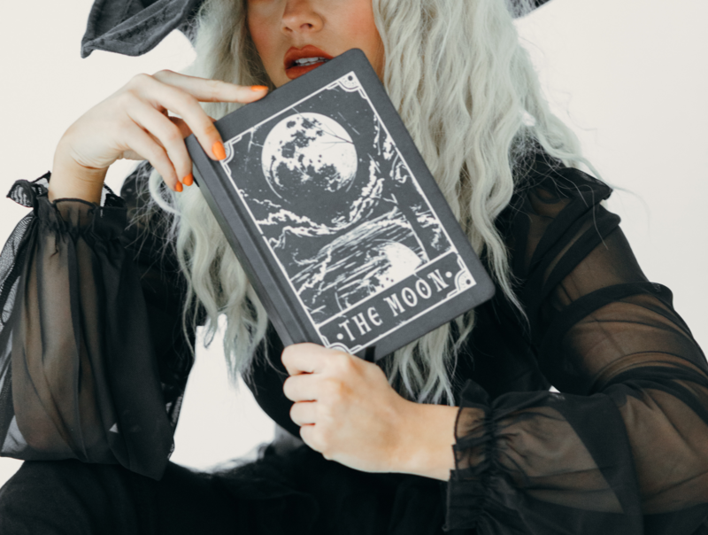 Silver haired witch in black clothes and hat  holding a moon book