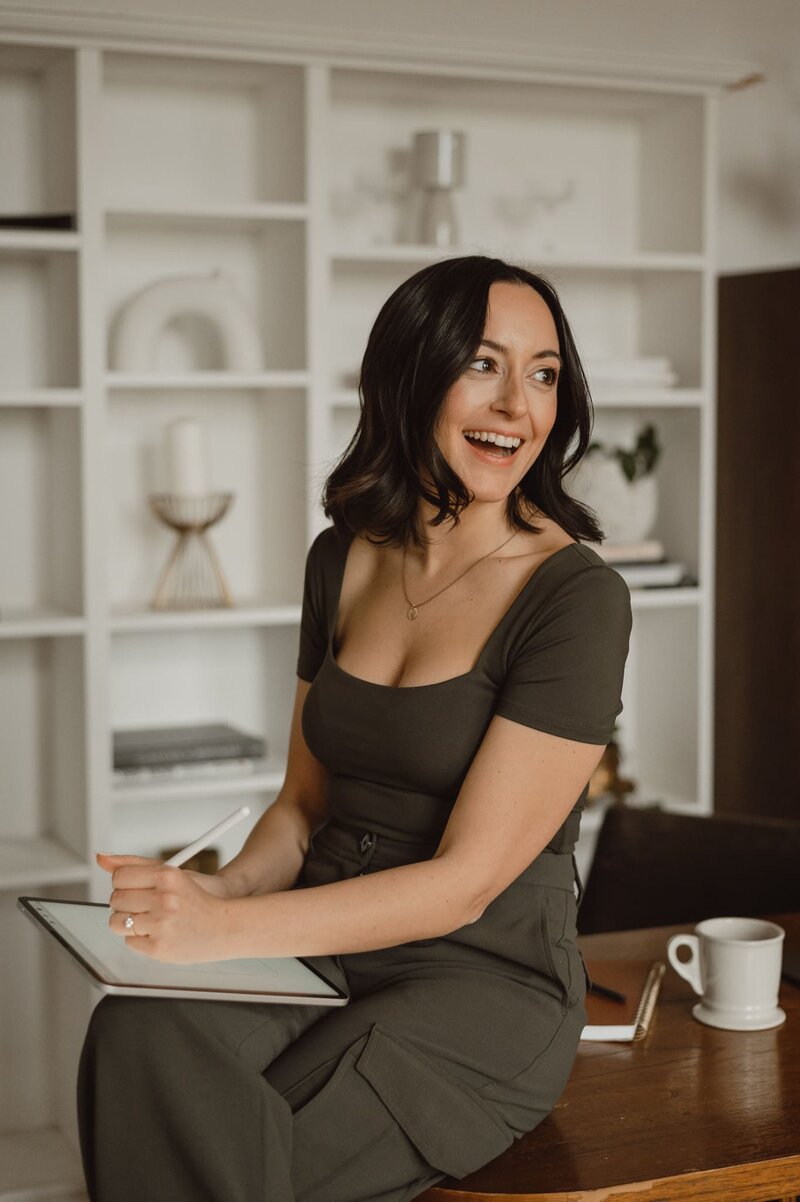 Vickie Chountalos of VERVE & COLOR sitting at a table, looking over her should and smiling.