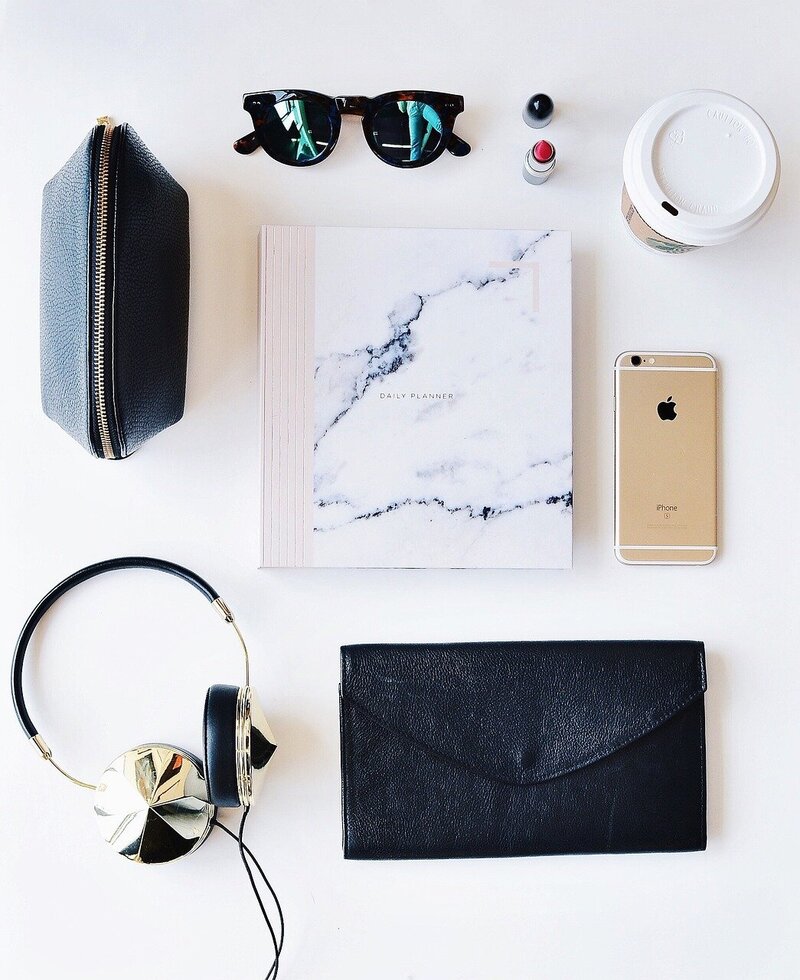 Flat lay of sunglasses, lipstick, coffee, and notebook—Emily Collins’ favorite everyday items.