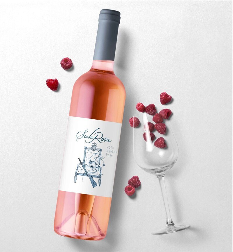 Bottle of Rose wine with Subrosa wine label design next to a wine glass and raspberries