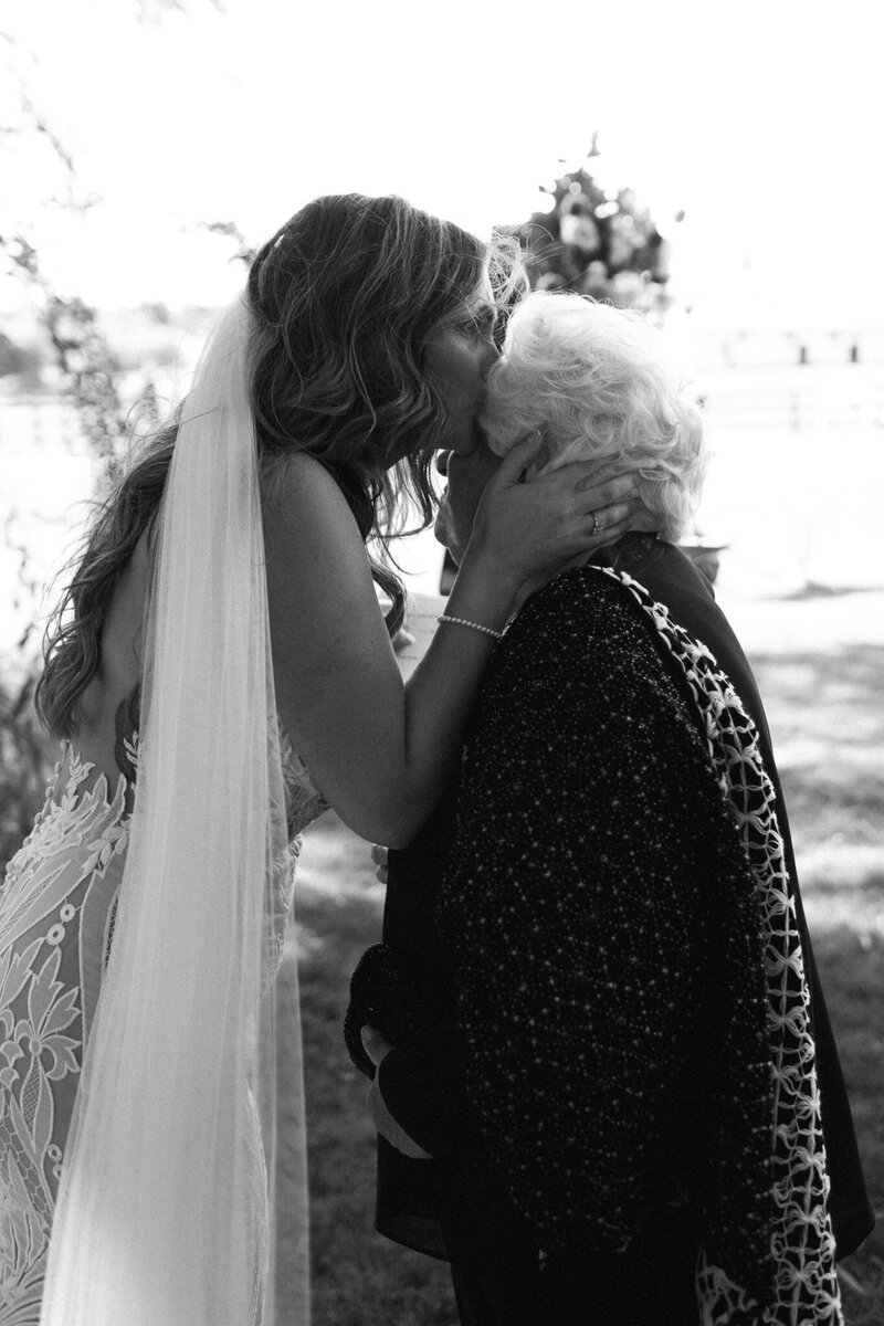 Bride in a wedding dress kisses an elderly woman with white hair on the forehead outdoors, captured beautifully by Caledon Valley wedding photographer, Jennifer van Son.