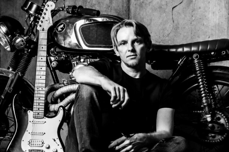 Music Artist Portrait Shaun Peace sitting beside old motorbike with electric guitar leaning beside him