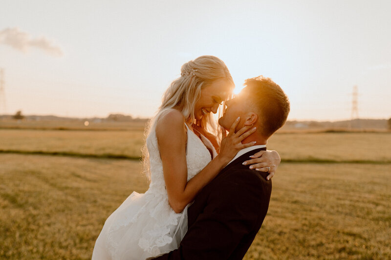 groom holding up bride in grass field