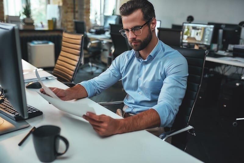 architect in blue button down reviews plans at office desk