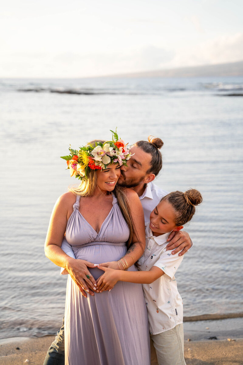 Family cuddling for maternity photos on the beach, taken by Big Island Photographer