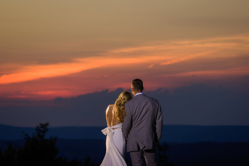 Couple leaning on each other with their backs to the camera, framed by a fiery summer sunset at the Blue Mountain lookout.