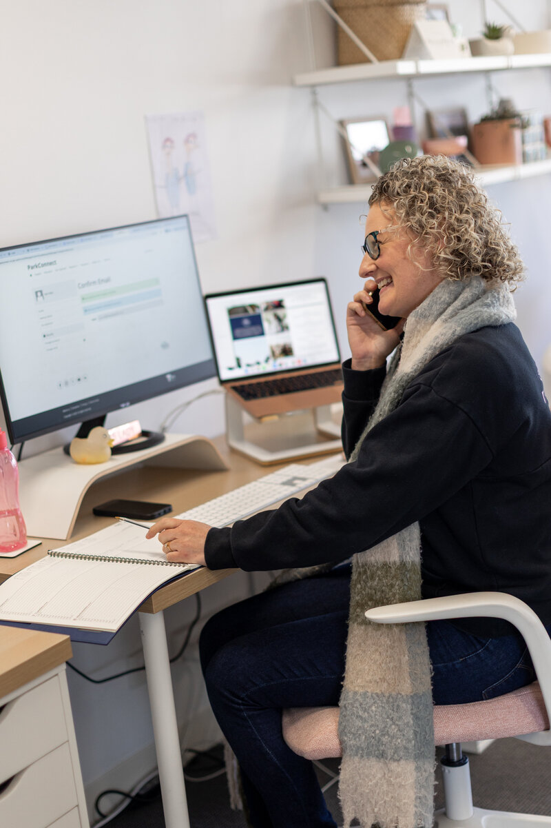 A woman holding a phone sitting at a desk with a computer