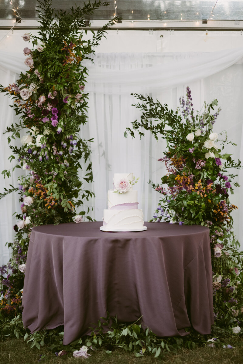 Incredible Wedding Cake Table with lush assymetircal arches and violet linen photo by mountainnaire gatherings