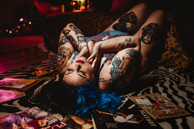 Baltimore photographers  captured boudoir pictures in studio session with tattooed woman laying on a variety of old school playboy magazines for unique boudoir pictures