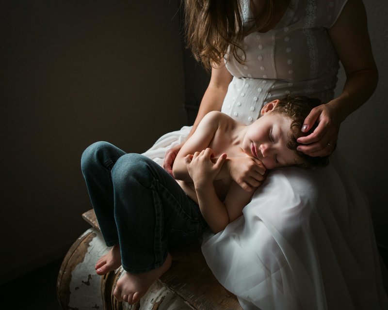 Sky 9 Studio  Mother lovingly strokes her 4 year old son's curly hair as he lays with his eyes closed on her lap during pregancy photoshoot