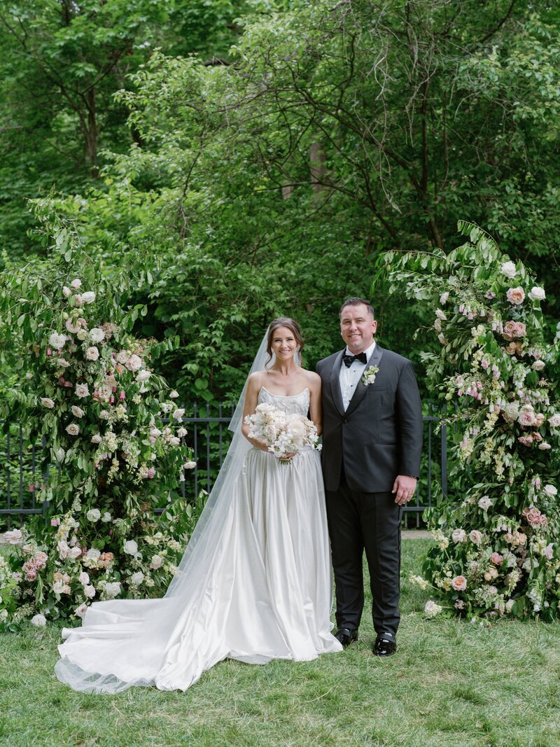 bride and groom posing in between two floral columns