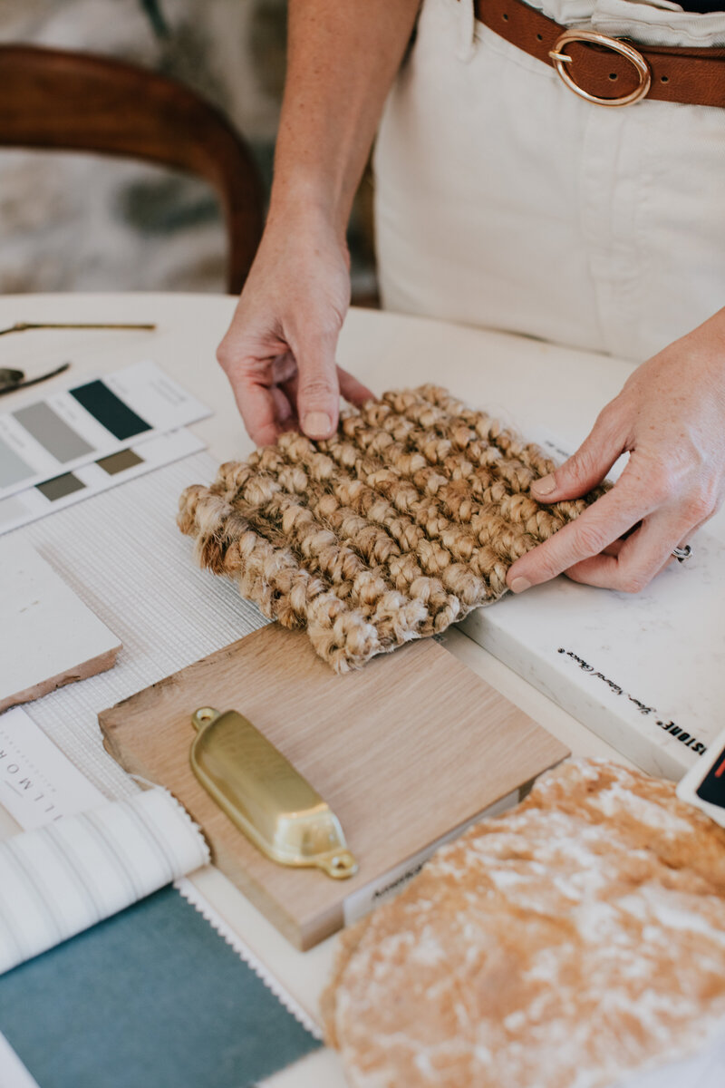 A luxury home design Newcastle expert examines a textured fabric sample on a table, surrounded by design materials and a cabinet handle, showcasing their finesse in creating elegant spaces.