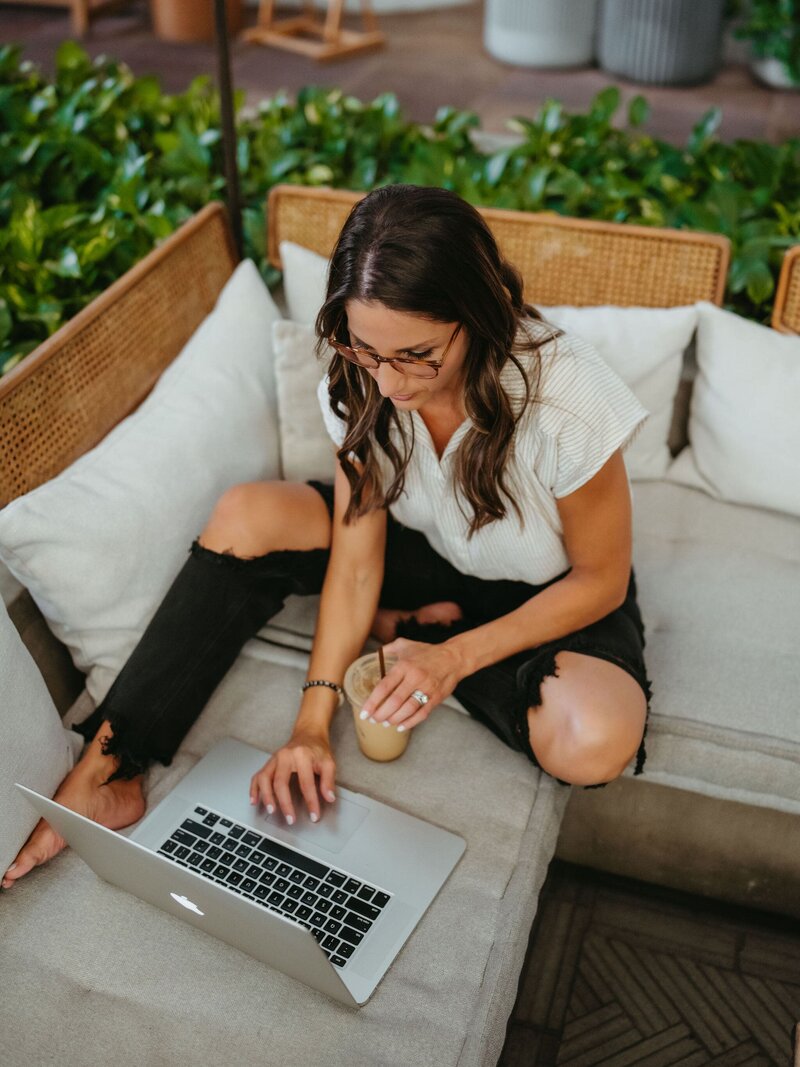 woman sitting on a couch with iced coffee working on laptop