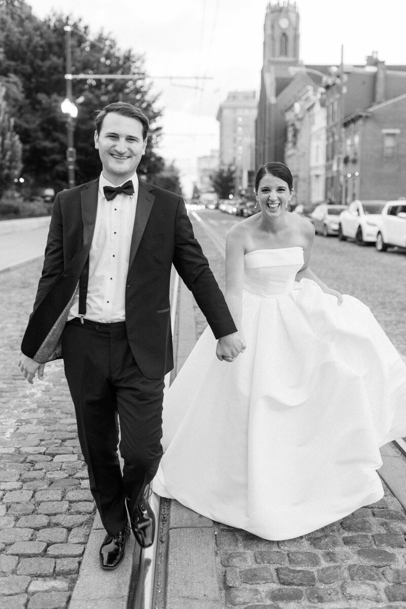 Black and white photo of a couple holding hands and running though the streets of downtown Cincinnati on their wedding day