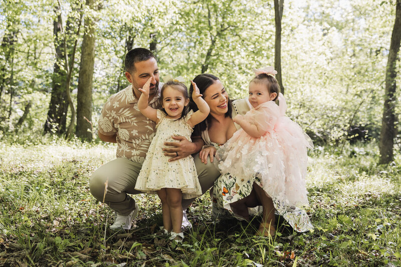 Parents crouching down in a wooded area smiling at their kids 