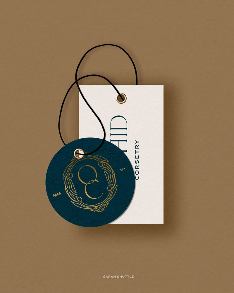 Branded swing tag mockups in teal and white placed on a gold background — identity by Sarah Shuttle Luxury Brands