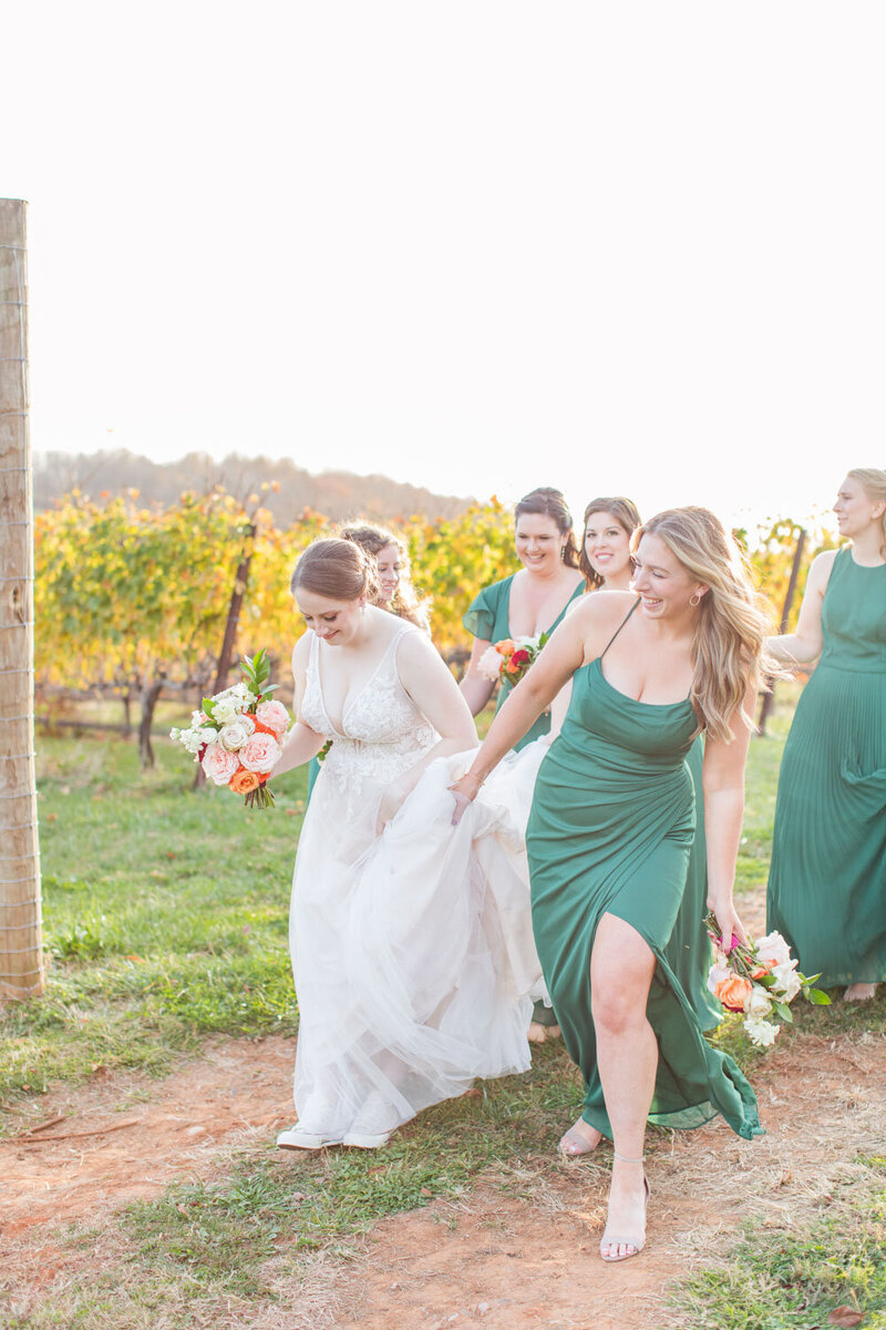 Bride walking with bridesmaids in green dresses through vineyard