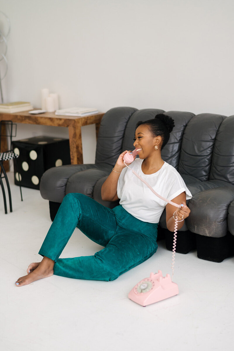 A woman sits on the floor while talking on a rotary phone