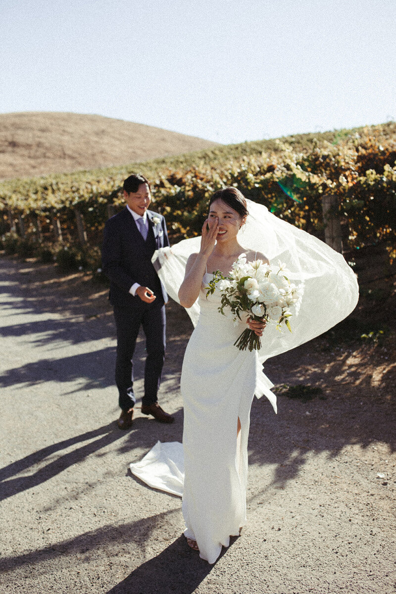 A bride wipes a tear away on her wedding day in Napa, CA while the groom holds her veil
