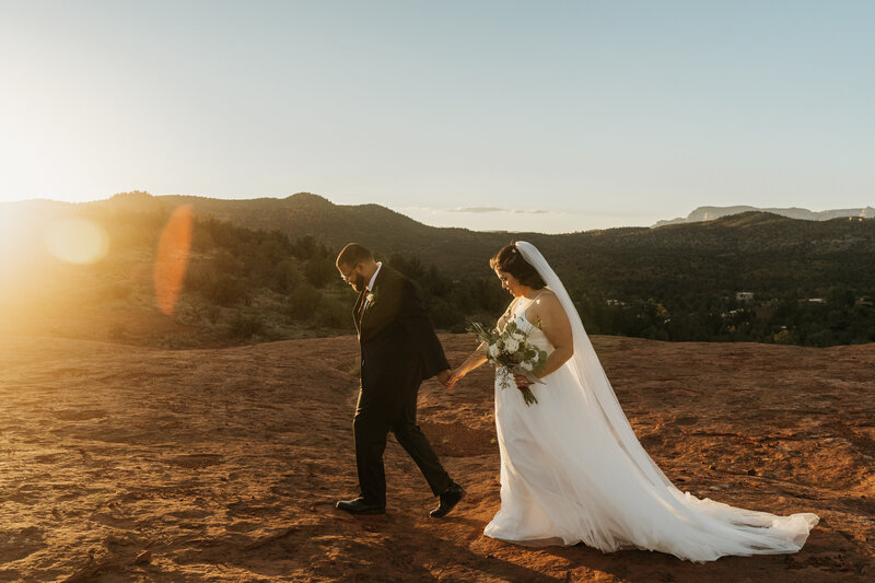 A newlywed couple holding hands and walking across a desert landscape 