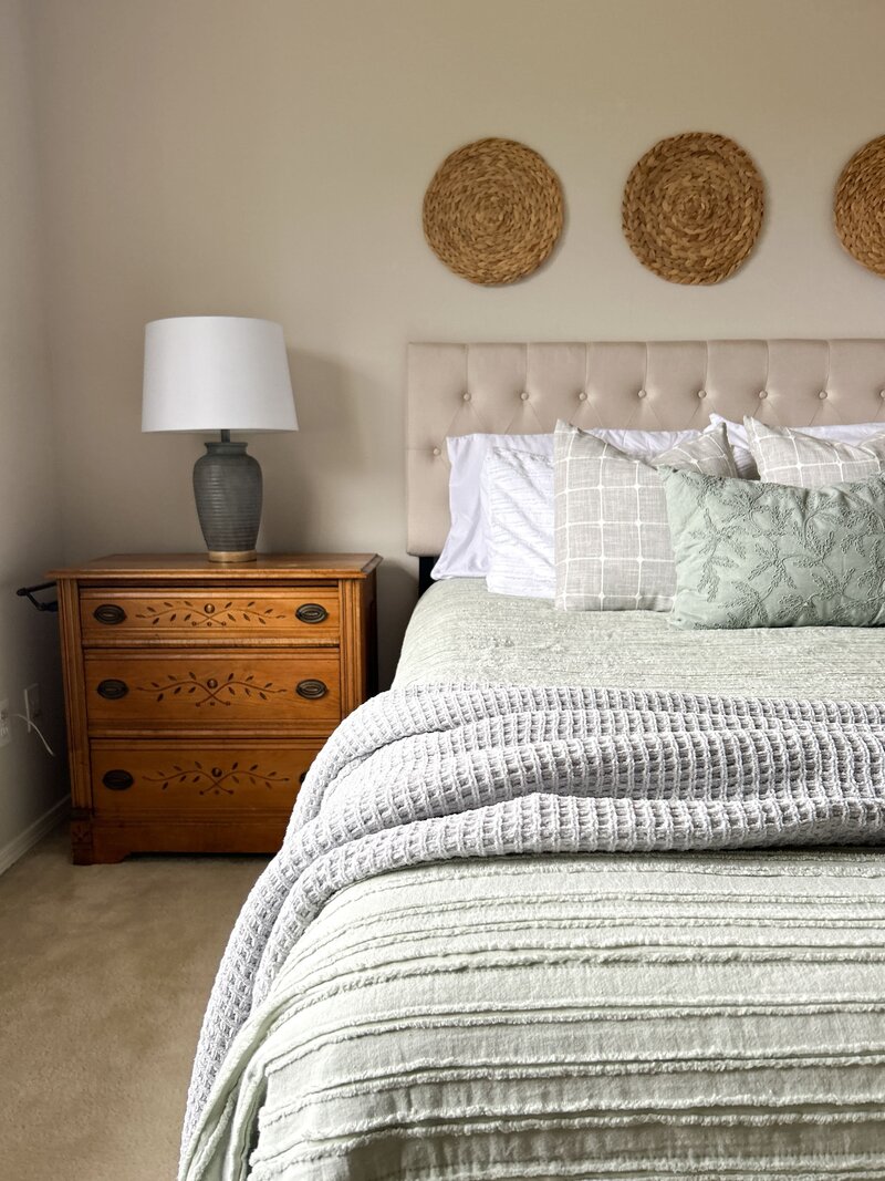Bedroom staged by Modern Mollusk in Snohomish County featuring soft green bedding, layered textures, and natural woven wall decor.