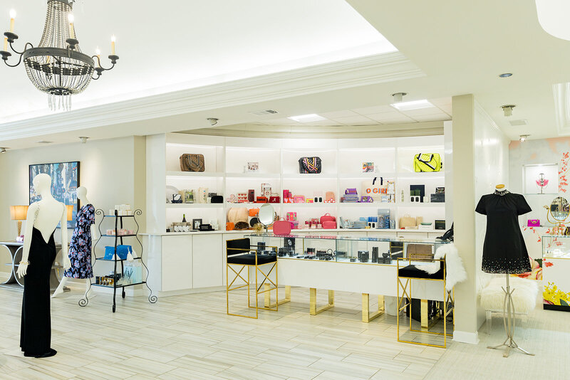 Elegant boutique in Columbia, SC, featuring designer handbags, beauty products, and accessories displayed on illuminated white shelves. Gold-accented furniture, mannequins in stylish outfits, and a crystal chandelier create a luxurious shopping experience. Small business branding photography in Columbia, SC, showcasing high-end retail and fashion branding.