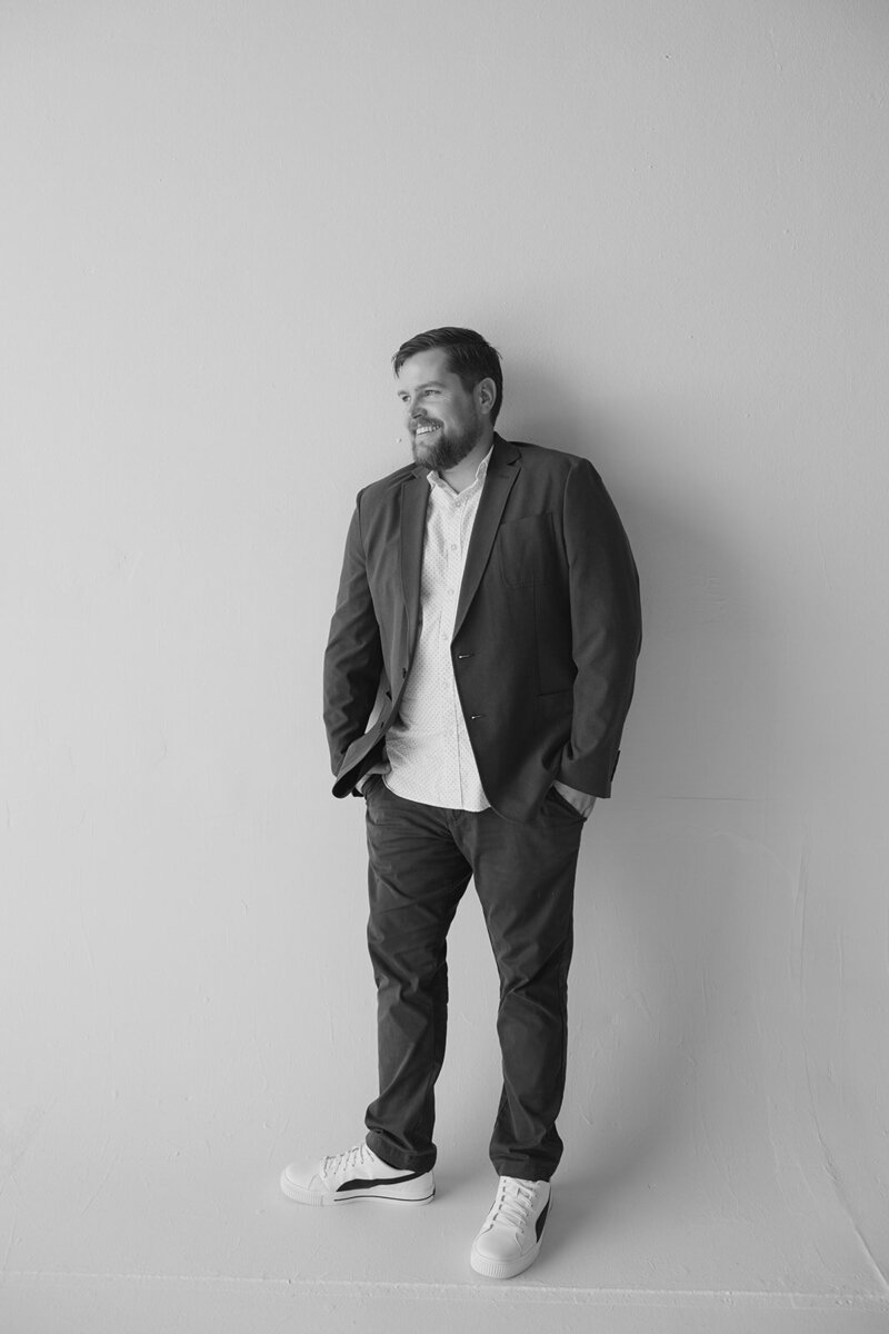 A well-dressed man in a suit paired with white sneakers leans against a wall, merging elegance with a modern twist.