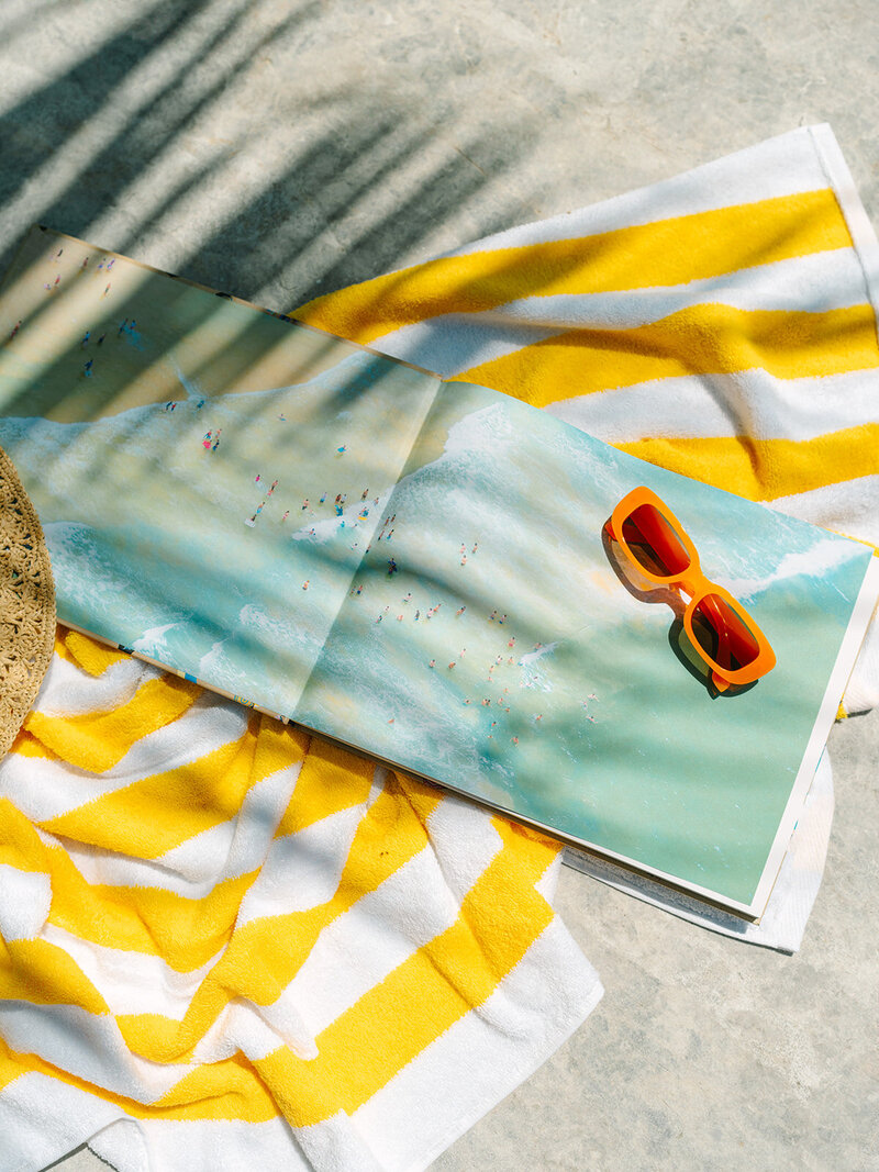 Book and orange sunglasses laying on a yellow striped towel