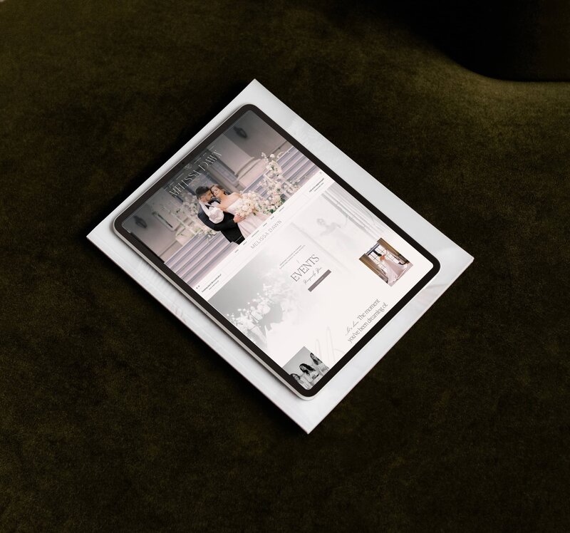 A tablet displaying a wedding-themed Showit website design lies on a white sheet, placed on a dark green surface.