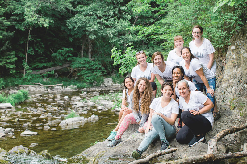 a group of small business owners gatehred on a rock beside a creek as part of a work-life balance retreat