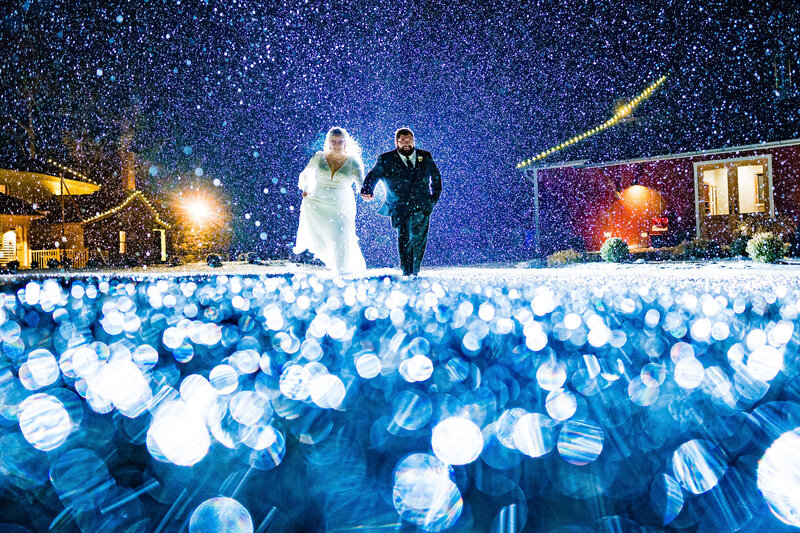 Wedding couple holding hands running towards the camera during a winter storm in Michigan