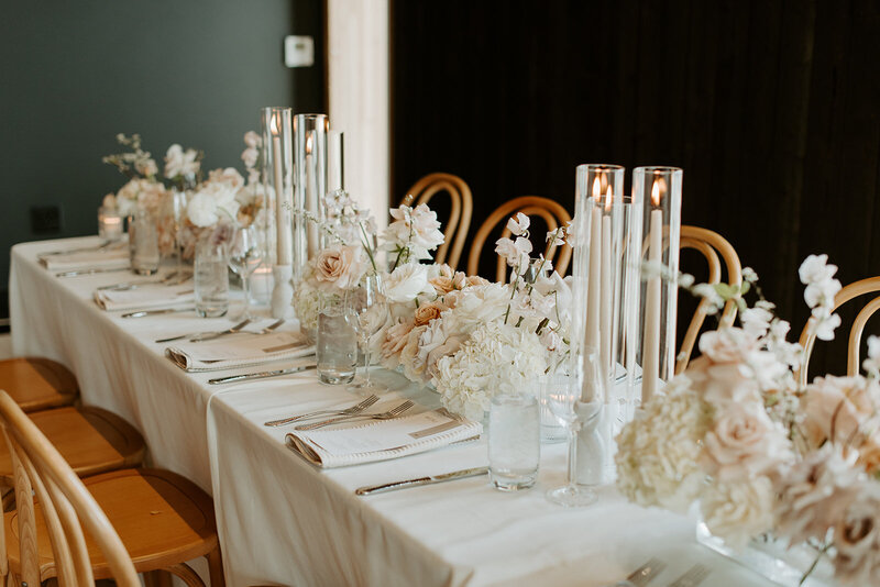 Reception tables with lucite vases of white and neutral-toned florals, pale Bentwood chairs, and candlelight at Jenay and Daniel’s modern romantic wedding, by Summer Robbins Flowers in Central Oregon