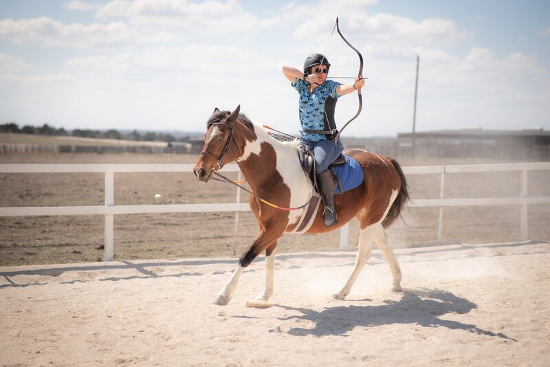 Woman Riding horse with arrow draw to shoot archery target while riding