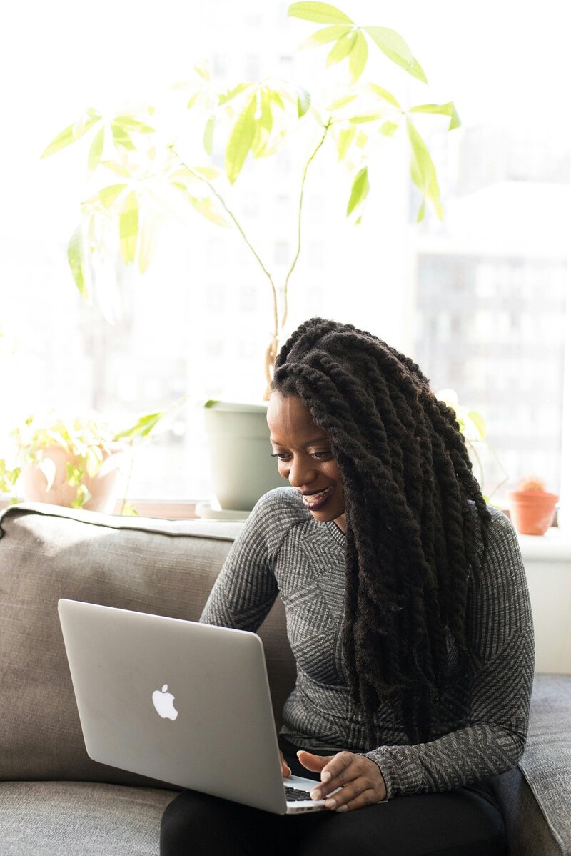 A black woman with long dreads smiles while using a computer