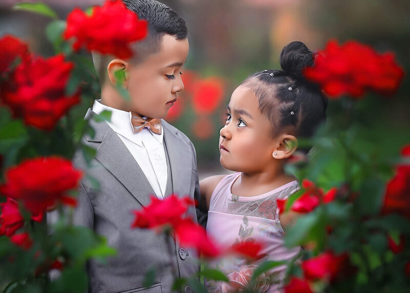 Brother and Sister in red roses posing at their denver childrens photography session.