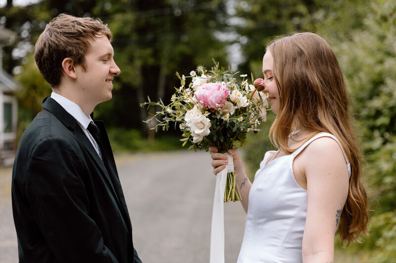 Couple facing each other, bride is sniffing flowers.