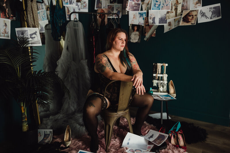 Woman sits in lingerie among fashion clippings, pearls, and shoes in styled studio boudoir session in Tampa, Florida.