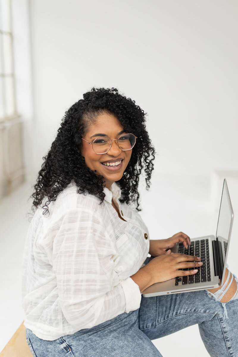 Alexa Luckenbach smiling while working on her laptop, designing strategic websites for female service providers and coaches