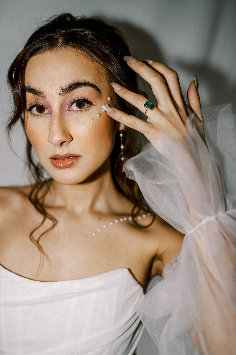 A woman holds her hand up to her face with decorative pearls on her skin, representing an artistic styled photoshoot by Among the Oaks. 