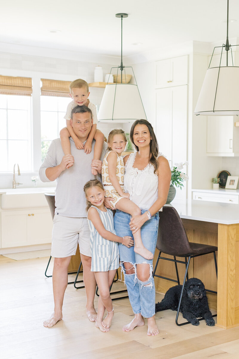 A happy family with three young children and their dog posing in a light-filled kitchen during their lifestyle session — Portrait photos in Raleigh.