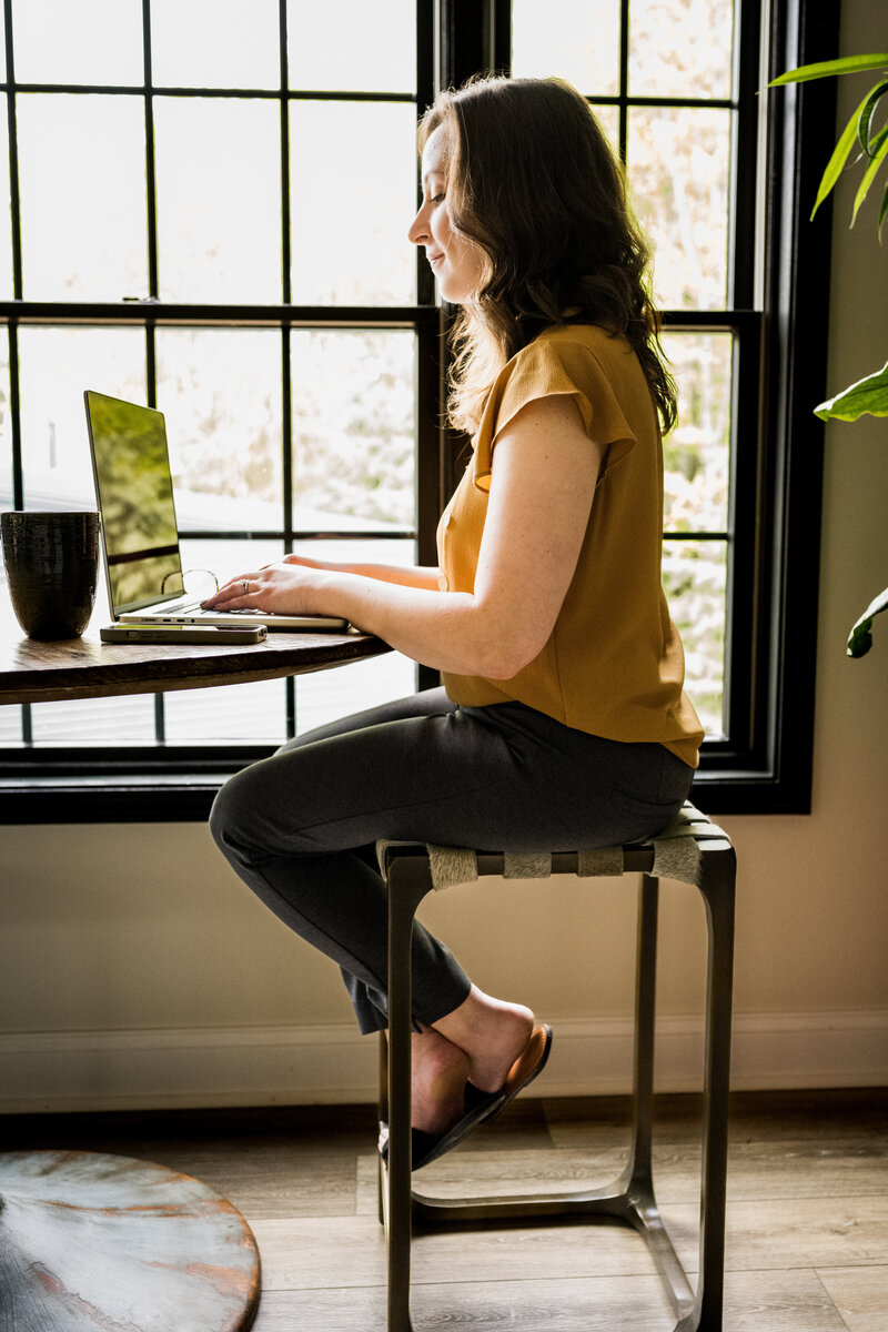 Melonie typing on a computer at a high table, working on an intentional and responsive web design for a health and wellness professional.