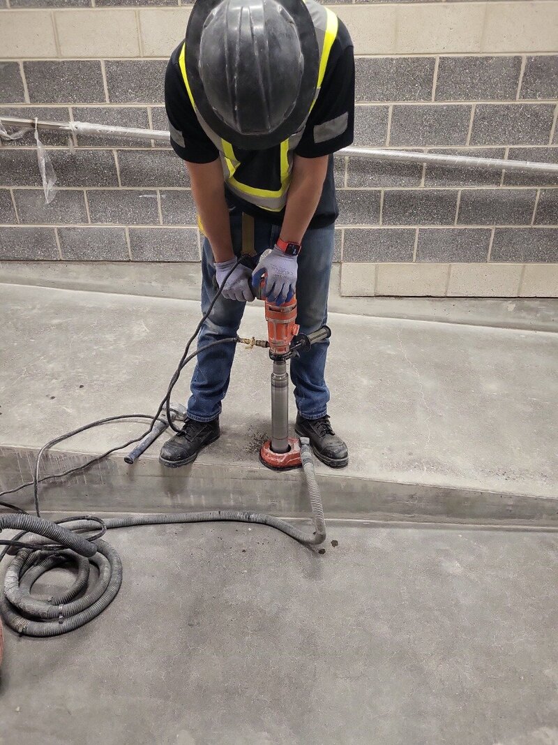 An operator works to core a hole in a section of  concrete while a vacuum removes all the mess that is created.