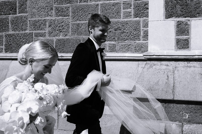 bride carries veil and groom walking past the arts centre in christchurch at their urban wedding