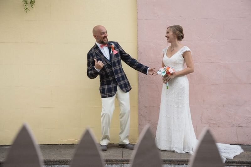 A couple shares a joyful moment on their wedding day with the groom striking a playful pose and the bride laughing bouquet in hand