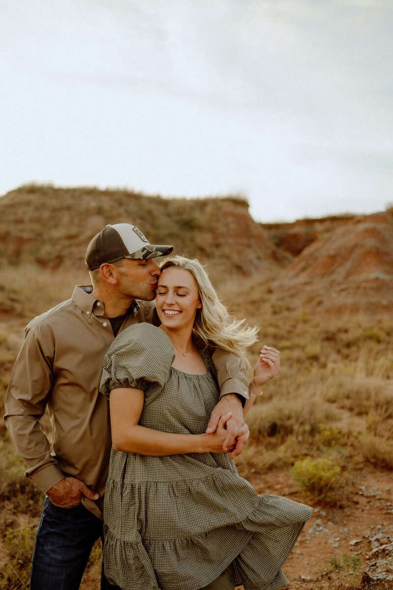 engagement photo of him kissing her on the temple while her hair blows in the wind