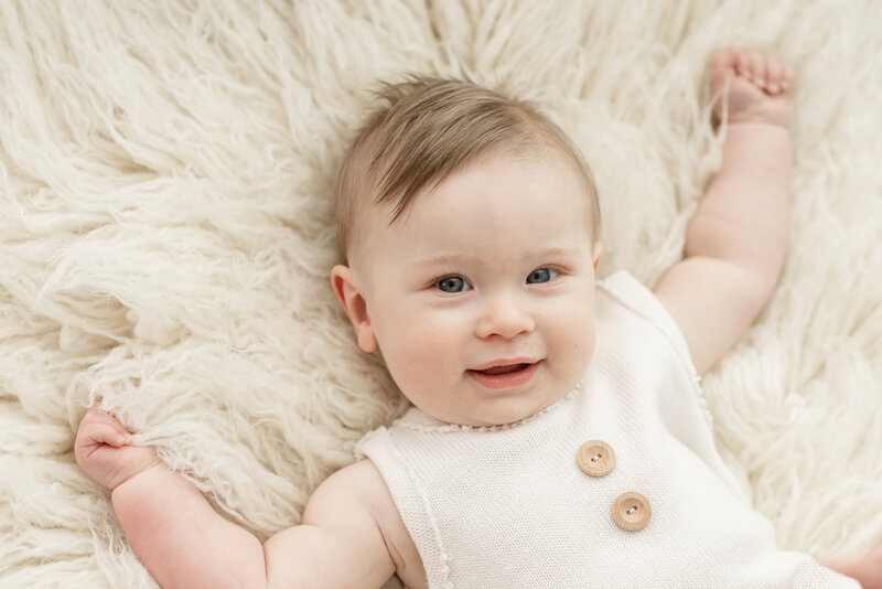 Six month old baby boy smiling at the camera, dressed in white