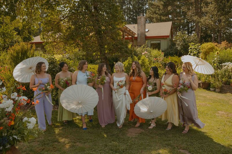 Bride with her bridesmaids smiling at each other holding paper umbrellas