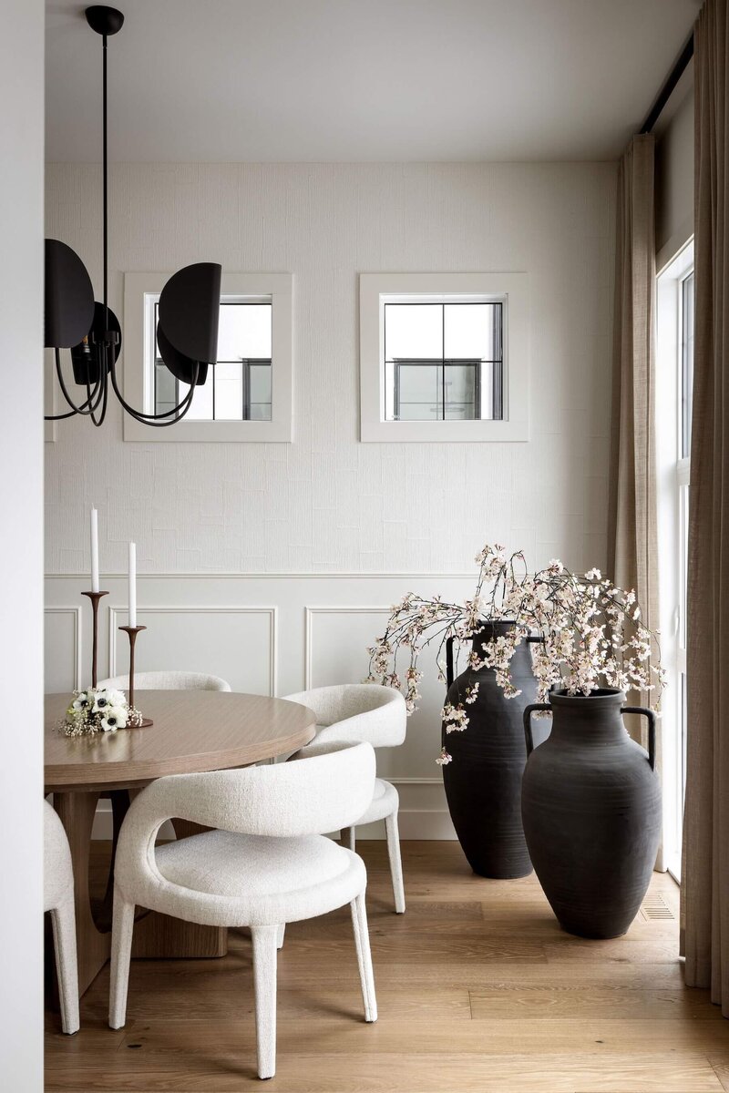 Minimalist dining space featuring a round table, black accents, plaster wall features and airy lighting that balance function with warmth and style.