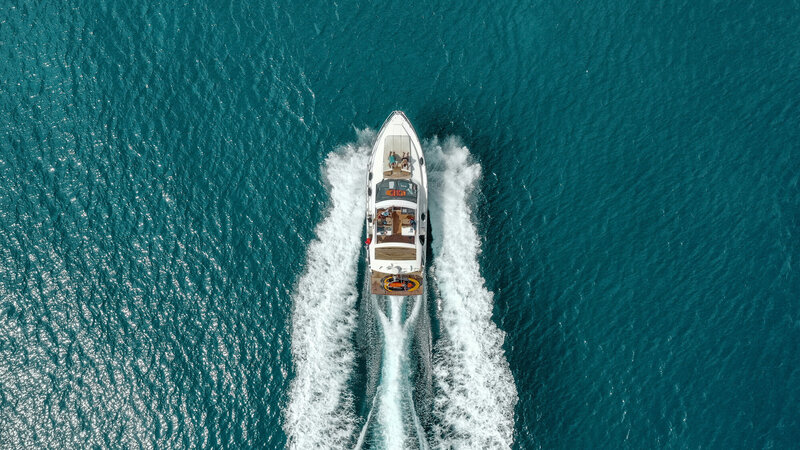 Aerial view of a yacht speeding through blue waters, creating a frothy wake behind it