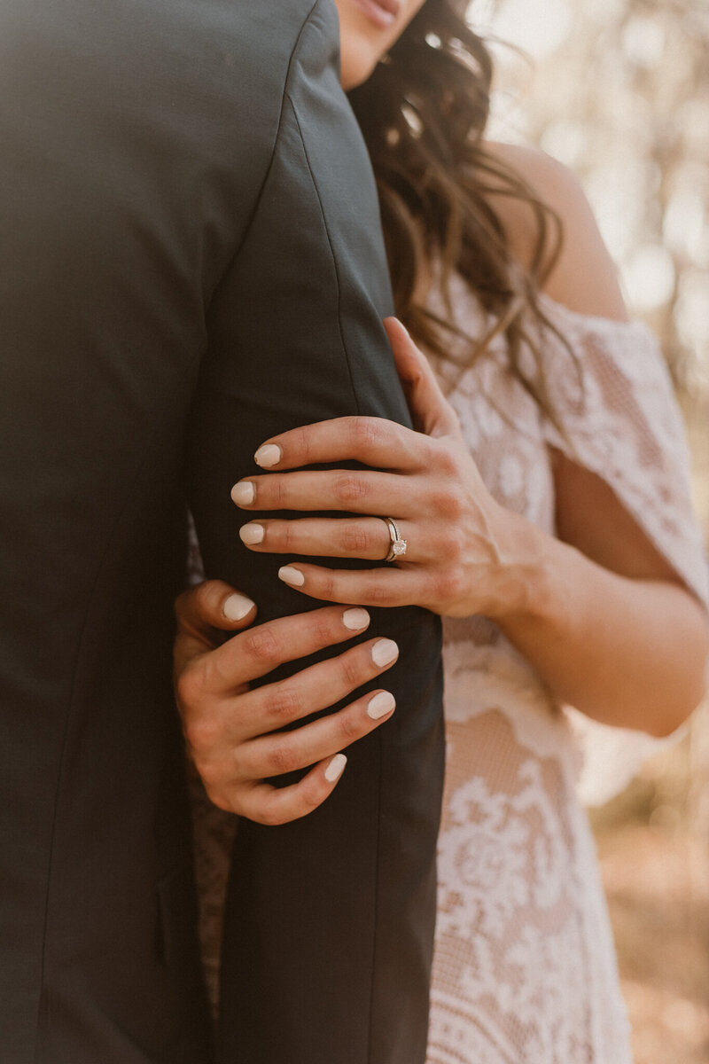 Close-up of a bride’s hand resting on the groom’s arm, showcasing her engagement ring and soft lace dress during an intimate elopement in Spring, Texas.